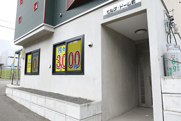 プラスルーム札幌ドーム前福住店の外観。窓に料金看板を掲げた屋内型トランクルームの建物