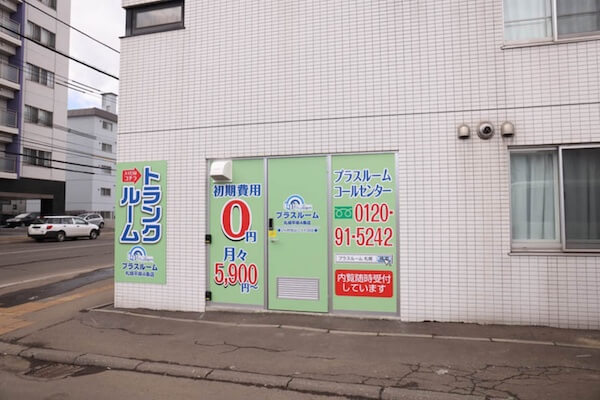 プラスルーム札幌平岸4条店の屋内型トランクルーム入口。初期費用0円の案内看板が並ぶ白いタイル外壁の外観