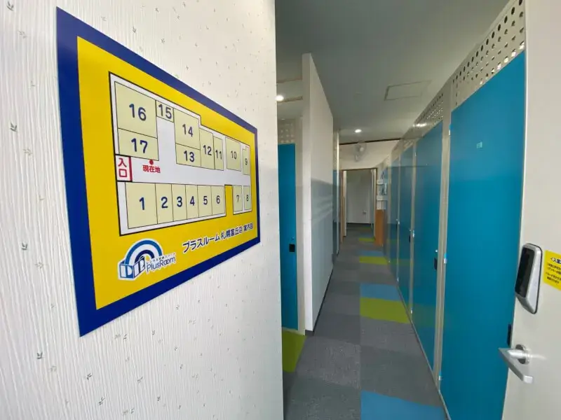 プラスルーム札幌富丘店の室内通路。青い扉のトランクルームが並び、壁の案内図で部屋の位置を確認できます